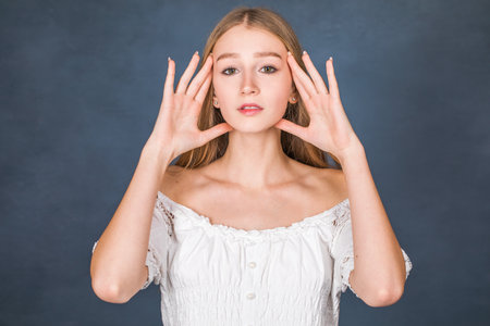 Close up portrait of a young beautiful blonde girl in white dress - isolated on blue backgroundの写真素材
