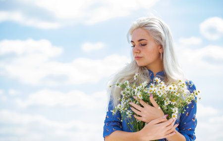 close up portrait of a young blonde girl with a bouquet of chamomile in a fieldの写真素材