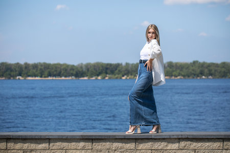 Full body portrait of a young beautiful blonde girl in long blue jeans skirtの写真素材
