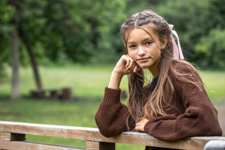Portrait of a beautiful teenage girl in a knitted brown sweater, summer park outdoorsの写真素材