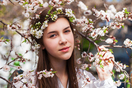 Pretty teen girl are posing in garden near blossom cherry tree with white flowers. Spring time