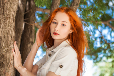 Portrait of a young beautiful redhair woman on the background of tree bark