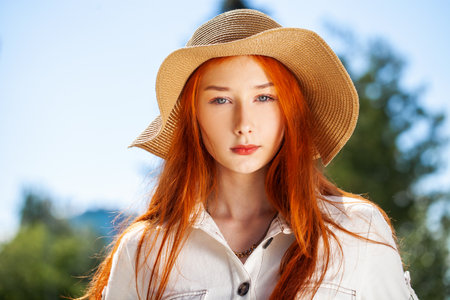 Close up portrait of a young beautiful girl in a straw hat posing in a summer parkの写真素材