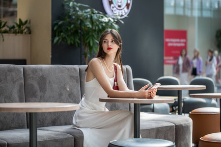 Portrait of a young beautiful girl sitting in a cafe with a mobile phoneの写真素材