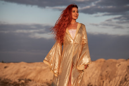 Oriental dance, young woman in golden dress against sunset background