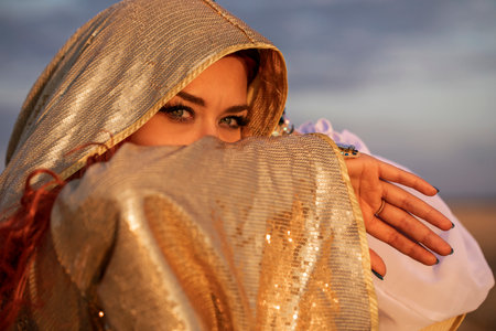 Oriental dance, young woman in golden hood against sunset background