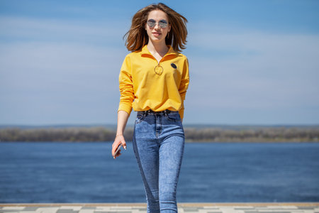 Young beautiful girl in blue jeans posing on the embankmentの写真素材