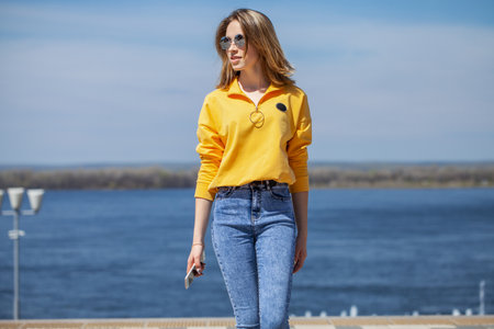 Young beautiful girl in blue jeans posing on the embankmentの写真素材