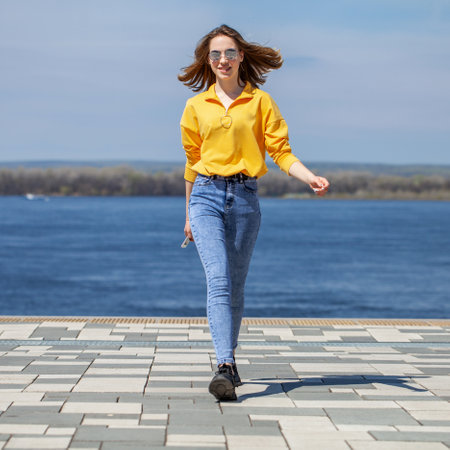 Young beautiful girl in blue jeans posing on the embankmentの写真素材