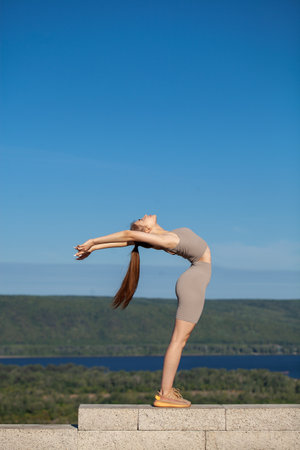 Fitness portrait young athletic woman doing gymnastics on blue sky backgroundの写真素材