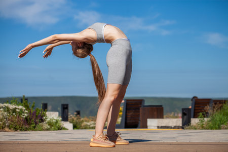 A young beautiful girl in a tracksuit performs physical exercises in a summer parkの写真素材