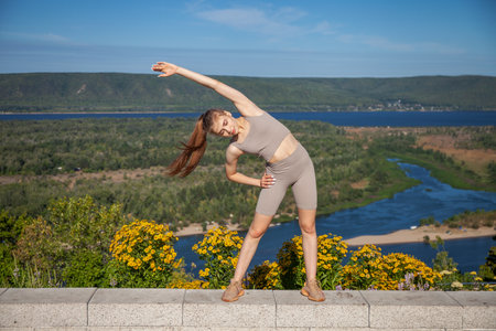 A young girl in a tracksuit performs physical exercises in a summer parkの写真素材