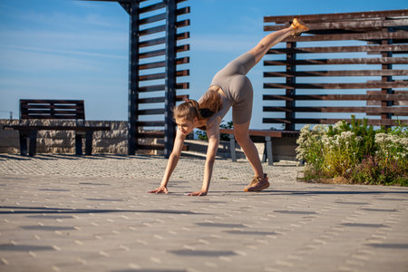 A young girl in a tracksuit performs physical exercises in a summer parkの写真素材