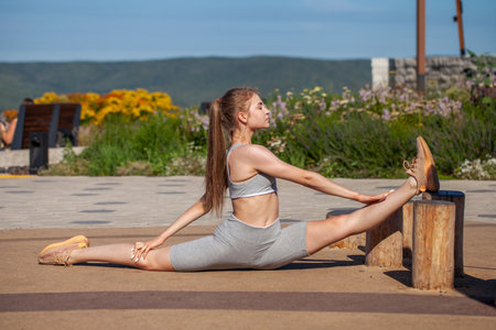 A young girl in a tracksuit performs physical exercises in a summer parkの写真素材