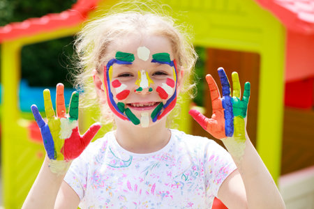 Little girl shows off her red-painted palms - smiling little student girl showing painted hands at school, summer outdoorsの写真素材