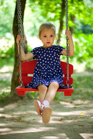 Adorable little girl having fun on a swing, against background of summer parkの写真素材