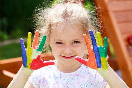 Little girl shows off her painted palms - smiling little student girl showing painted hands at school, summer outdoorsの写真素材