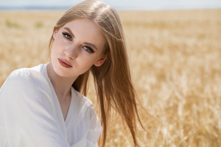 Portrait of a young beautiful blonde girl posing in a wheat fieldの写真素材