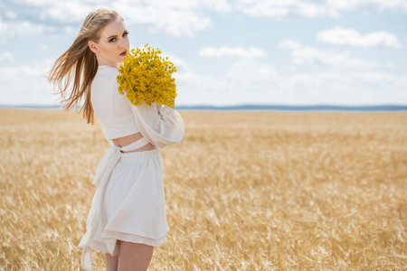 Portrait of a young beautiful blonde girl posing in a wheat fieldの写真素材