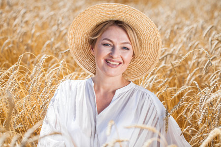 Portrait of a middle-aged woman in a straw hat posing in a wheat fieldの写真素材