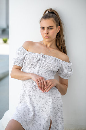Portrait of a young beautiful brunette girl in a white summer dress with open shouldersの写真素材