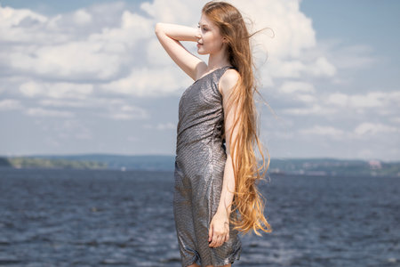 Young blonde girl posing in silver tight dress on the river bankの写真素材