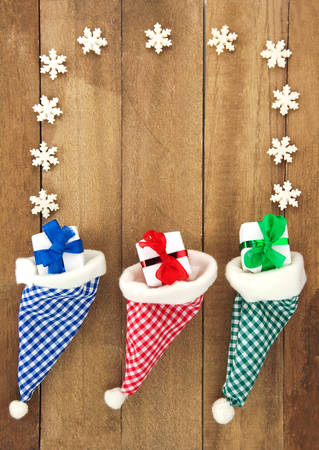 Three red, green, blue and white checkered Santa hats with candy, gift, nuts and Christmas decoration on a rustic wooden background for Christmas or St. Nicholasの写真素材