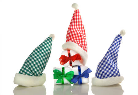 Three red and white, blue and white and green and white chequered santa hats and three white gifts with coloured ribbons isolated in front of white backgroundの写真素材