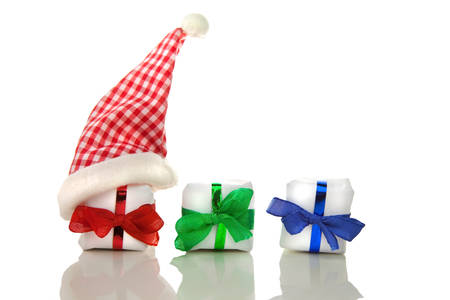 Three white christmas packets with coloured bows and chequered santa hat in front of white backgroundの写真素材