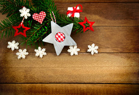 Rustic brown wooden background decorated with green fir branch, red and red and white checkered stars and santa hat, gift and snowflakes as Christmas decoration in Country Styleの写真素材