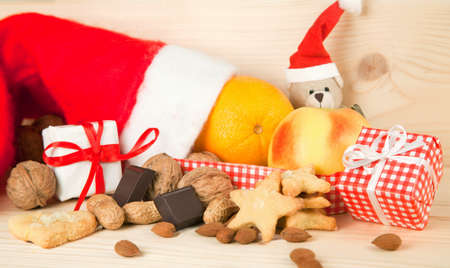 Christmas fruits and Nicholas gift consisting of a Santa Claus hat with cookies, biscuits, walnuts, hazelnuts, almonds, oranges, apples, chocolate, gifts and Christmas decoration isolated against white backgroundの写真素材