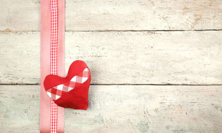 Rustic wooden wall with red and white checkered heart made of cloth and checkered ribbon as greeting cardの写真素材