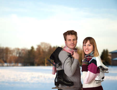 happy smiling young woman and man outside on snow winter day holding ice skates outdoorsの写真素材