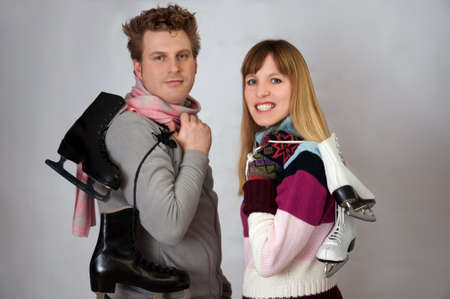 Young woman and man holding ice skates for winter sport in front of grey background の写真素材