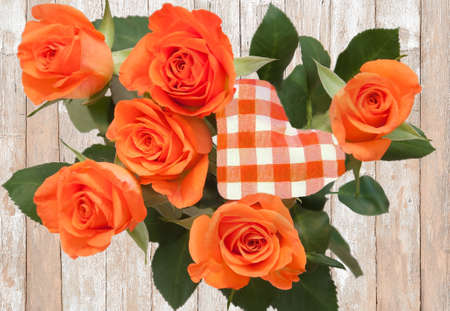Still life with orange rose bouquet with red and white checkered cloth heart on boards of wood の写真素材