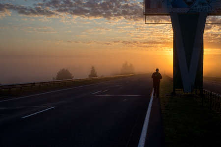 The road in the morning fog and dawn on the highway, the rising sun illuminates the pathの写真素材