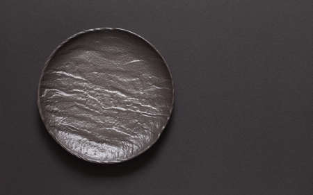 Dark grey textured concrete background for design with black food plate. Copy spaceの写真素材