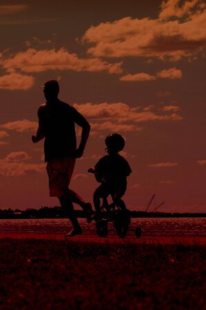 Man and child running at sunset silhouetted on beachの写真素材