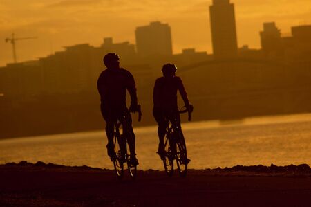 Silhouetted exercisers against an orange sky along the river cityの写真素材