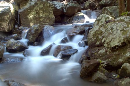 smooth white water flowing over bush rocksの写真素材
