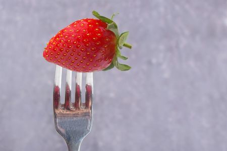 a single strawberry on a silver forkの写真素材