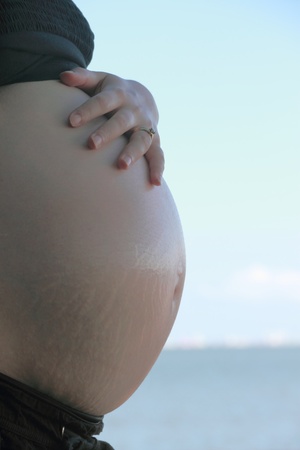 pregnant woman holding stomach outdoors on beach
