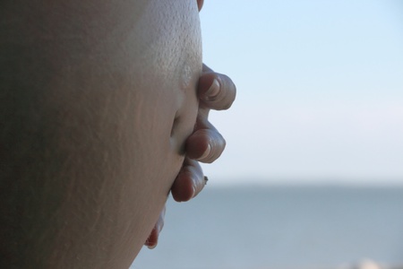 pregnant woman holding stomach outdoors on beachの写真素材
