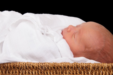 baby in wicker moses basket isolated over blackの写真素材