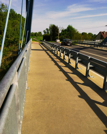 A vertical photo of a modern bridge with a black car and a white car driving on itの写真素材