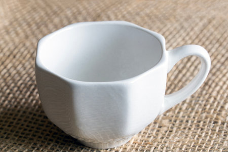 A white octagonal coffee cup stands on a jute fabric