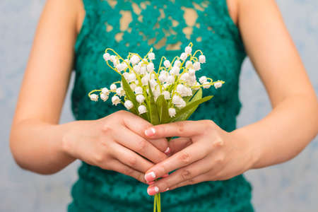 Elegant slim girl holds out lilies of valley, on blue backgroundの写真素材
