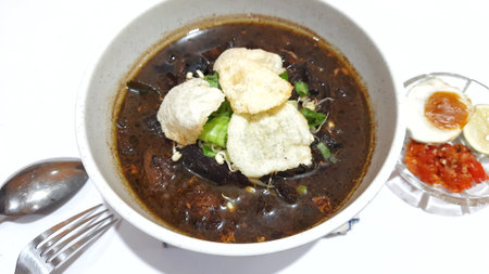 Black meat soup Rawon with leeks, bean sprouts and crackers in a white bowl isolated on white backgroundの写真素材