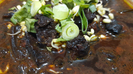 Black meat soup Rawon with leeks and bean sprouts crackers in a white bowl isolated on white backgroundの写真素材