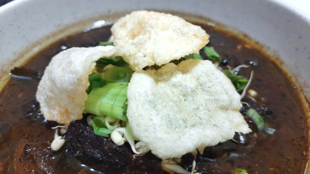 Black meat soup Rawon with leeks, bean sprouts and crackers in a white bowl isolated on white backgroundの写真素材